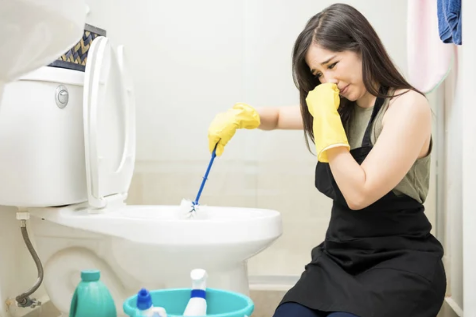 A woman on her knees cleaning a toilet that smells bad
