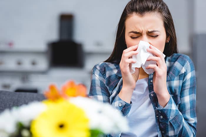 A woman blowing her nose due to allergies
